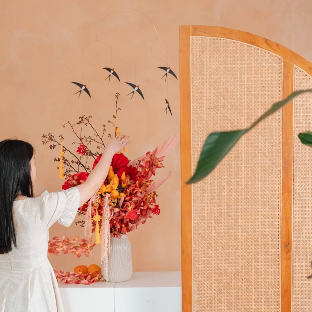 A woman in a white dress adjusting a vibrant Chinese New Year flower arrangement featuring red orchids, pussy willows, and gold ornaments